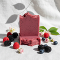 Berry Breeze goat milk soap bars styled with fresh raspberries, blackberries, blueberries, and soft florals on white linen with dappled sunlight