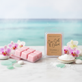 Sea Salt & Orchid wax melt clamshell packages displayed on white marble with fresh pink and white orchids, sea glass, smooth pebbles, and sea salt crystals with a soft turquoise ocean in the background