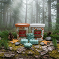 Balsam Fir wax melt buckets close-up on a mossy log in a lush evergreen forest with fresh fir branches, pine cones, river stones, and soft misty forest light in the background