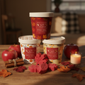 Apple Cinnamon wax melt buckets displayed on a rustic wooden surface with fresh red apples, cinnamon sticks, deep red maple leaves, and a warm glowing candle in rich autumn tones